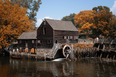 An autumn view of the grist mill at Philipsburg Manor restoration in Sleepy Hollow. People stand on a dock while water runs under the mill wheel.