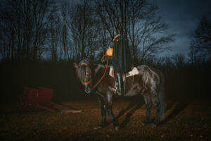 The headless horseman holds a pumpkin in a farmyard at night.