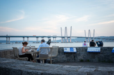 A couple seated at the observation deck at Pierson Park in Tarrytown, New York, with Mario Cuomo Bridge in background.