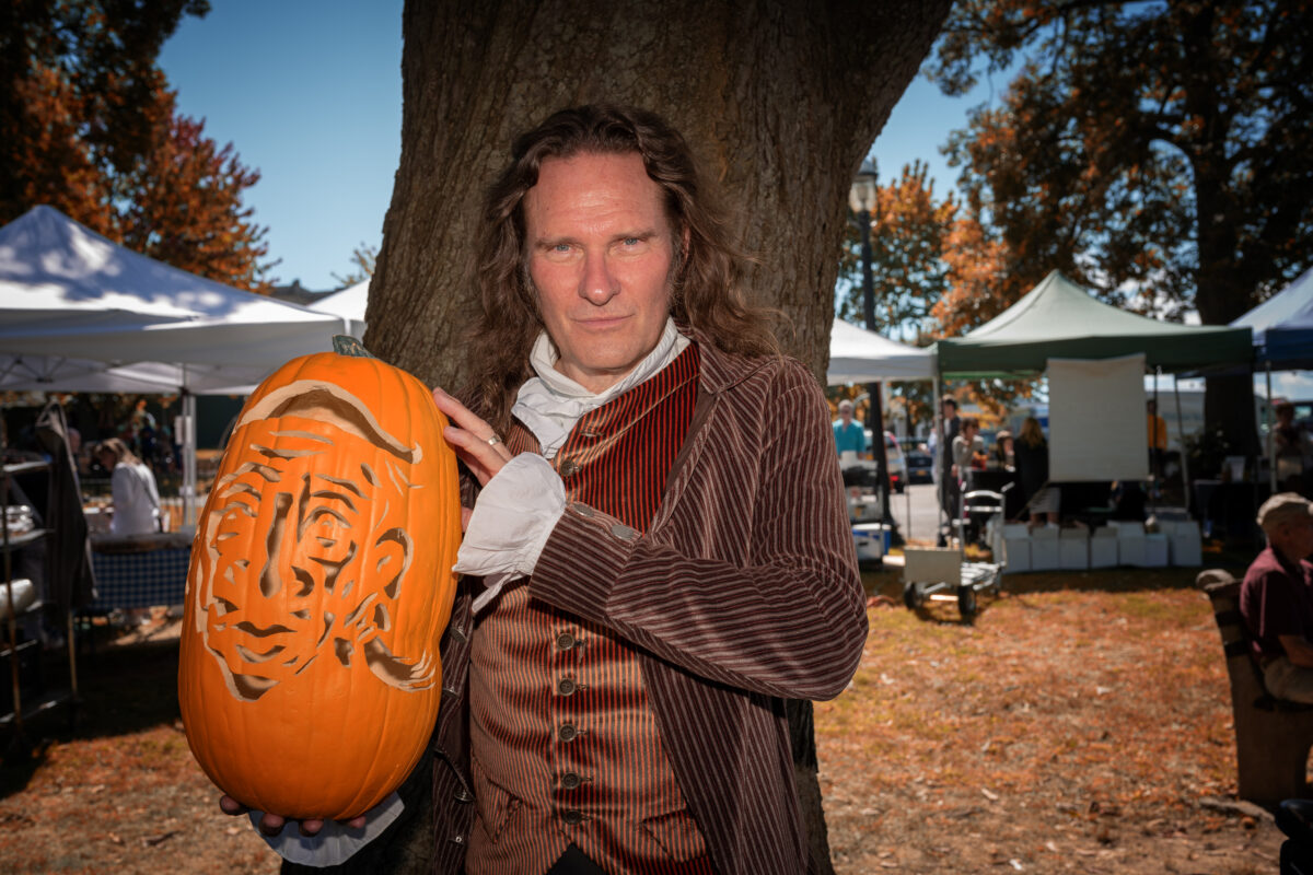 Storyteller Jonathan Kruk holds a carved jack-o'-lantern at a farmers market.