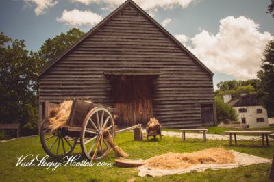 A cart filled with sheaves of wheat stands in front of Philipsburg Manor's colonial era barn.