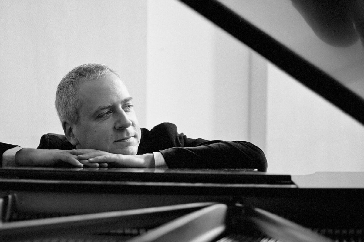 Pianist Jeremy Denk leans on a grand piano in this press photo.